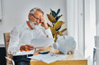 © Carlos David - Portrait of a senior white hair man at home desk worried about money, contracts and paying bills or loans