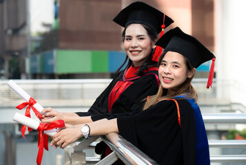 Two graduate women in graduation gowns hold diplomas have happy and success on university campus, Graduate with diploma. Graduate feeling happy after receiving long awaited master diploma.