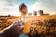 © Davide Angelini - Young woman holding boyfriend's hand walking in the field on sunset - Traveling together. Follow me.