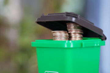 A model of a green trash can with dollar coins coming out of the lid