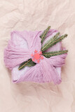 Fototapeta Storczyk - gift wrapped in pink textile with fir branches on beige background.