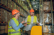 © zinkevych - Warehouse workers in orange helmets standing in the aisle and talking