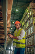 © zinkevych - Warehouse worker in yellow vest checking boxes on the shelves and smiling