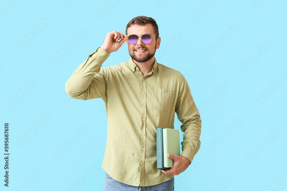 Handsome man with stylish sunglasses and books on color background
