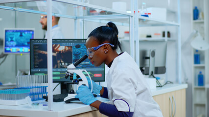 african scientist checking sample of virus using microscope in modern lab. multiethnic team examinin