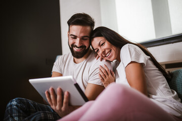 Wall Mural - Smiling relaxed young couple using digital tablet in bed at home