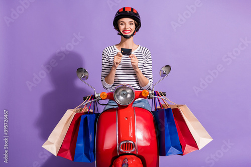 Plakat Photo of adorable driver woman wear striped outfit red helmet sitting bike holding bank card isolated violet color background