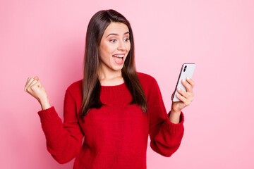 Poster - Photo of cute young girl hold smartphone raise fist open mouth wear red sweater isolated pink color background