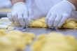 Handmade pasta preparation - woman’s hands, with nylon gloves on, creating a candy shape from pasta with a cheese stuffing.