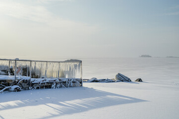 Wall Mural - a pier on the shore of a frozen bay. sunny winter day on the shore.
