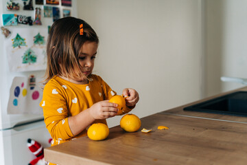 Caucasian girl peeling tangerines on kitchen counter. Healthy child diet. Immune boosting with vitamin c