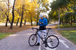 © Andrii Lysenko - a young man of European appearance is standing in a park on the paving stones near a bicycle and is typing on his smartphone.