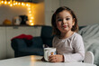 © troyanphoto - Caucasian toddler girl drinking cocoa from mug at home. Christmas bokeh lights