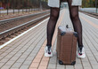 © Radnatt - woman in gray coat and with a suitcase stands at railway station. legs closeup