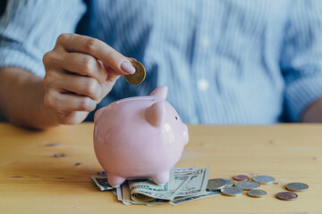 the woman's hand puts a coin in a pink piggy bank standing on the table. Concept of saving money or savings, investment during the global crisis