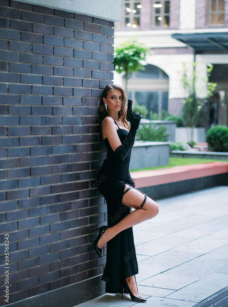 Beautiful young happy glamorous woman in a black evening dress with a gun  in her hands.