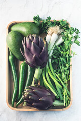 Wall Mural - Fresh vegetables and herbs on a wooden tray: Artichokes, parsley, avocado, green  onions and hot peppers. Healthy food concept