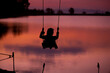 © K.Pornsatid - Silhouette of woman Ride on the swing By the lake Twilight