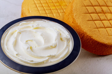 Close up of white icing in bowl with round sponge cake.