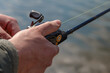 © mitsyko1971 - hand with spinning and reel on the evening summer lake. Fishing on the lake at sunset. Fishing background.