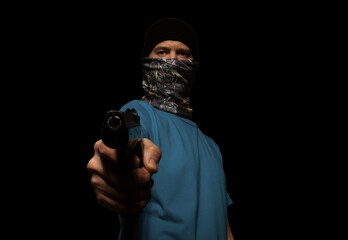 Wall Mural - A criminal man in a mask on his face, aiming a gun at a camera, on a black background