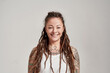 © Svitlana - Portrait of young tattooed caucasian woman with dreadlocks wearing white shirt, smiling at camera while posing isolated over grey background