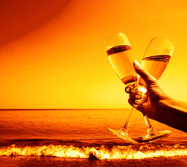 Female hand holding two 2 glasses of champagne against sea waves at evening. Selective focus, blurred background, space for text. empty copy space