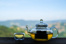 Glass Tea Pot And Tea Cup On Wooden Background Above Green Natural Mountain And Landscape Background. 