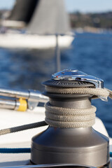 Winch locked, and loaded with sheet on a sailboat with diffuse view of water and land as selective focus background