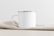 © Snoflinga - Enamel mug mockup with a table cloth on a beige table.