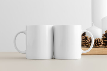 Two white mugs mockup with candles on a table. Christmas decoration