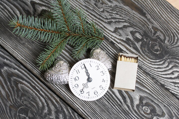 Two heart-shaped candles and fir branches. Watch dial. On black pine boards.