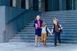 © Iryna - Happy pupil preteen girl and her two friends are going to school. Three different age kids running downstairs outdoors with school building on background. Happy childhood, back to school concept.
