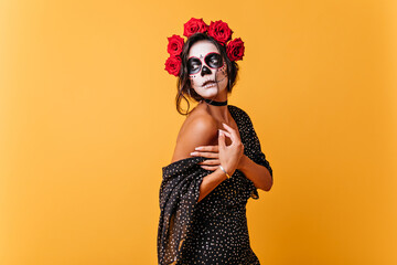 Wall Mural - Romantic girl gently holds falling dress. Lady with make-up in form of skull for carnival mysteriously looks away