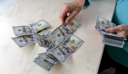 Close-up of an elderly woman's hands holding money in 100 dollar bills