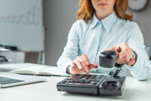 Cropped View Of Businesswoman With Handset Dialing Number On Landline Telephone At Workplace On Blurred Background