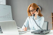 © LIGHTFIELD STUDIOS - businesswoman talking on landline telephone, while writing in notebook at workplace on blurred foreground