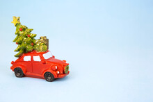 Christmas Decor - A Red Retro Car Carries A Christmas Tree With Gift Boxes On The Roof. Toy With Sequins On A Blue Background, Space For Text. New Year