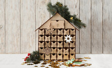 Wooden House Shaped Advent Calendar, Christmas Cookies And Festive Decor On White Table