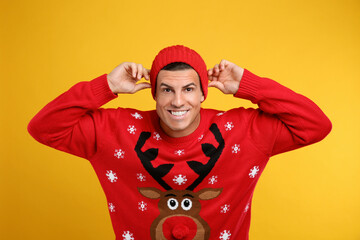 Wall Mural - Happy man in Christmas sweater and hat on yellow background