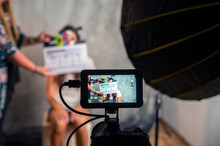 Operator Holding Clapperboard During The Production Of Short Film Inside A Studio With Young Actress On Stage. Blur Effect On The Clapperboard And Focus On Monitor. 