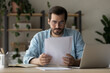 © fizkes - Thoughtful young Caucasian man sit at desk at home office read postal paper letter. Pensive millennial male get message or notice in paperwork or postal correspondence, consider banking document.