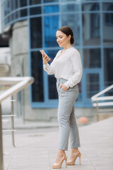 business woman walking on the street in the business district, checks her smartphone.