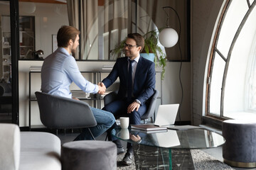 Canvas Print - Happy satisfied millennial men client and insurance broker handshaking after signing deal, friendly boss getting acquainted with new worker, young male intern thanking colleague mentor for assistance