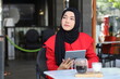 © Akarawut - Muslim girl wearing Islamic hijab sitting in outdoor cafe with hot coffee while using digital tablet with serious worrisome face