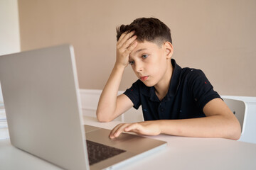 Schoolboy boy sitting at a desk with a laptop, writes school lessons during homework. High quality photo