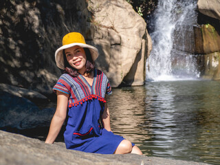 Wall Mural - Women wear traditional Thai costumes and yellow hats. Sitting by the waterfall