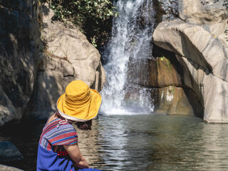 Wall Mural - Women wear traditional Thai costumes and yellow hats. Sitting by the waterfall