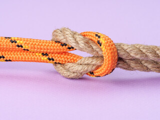 A square knot of nylon orange and hemp rope on a pastel purple background.