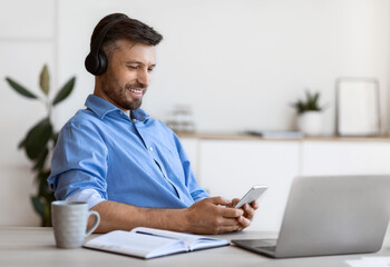 Handsome businessman listening music on smartphone with headphones while working at office